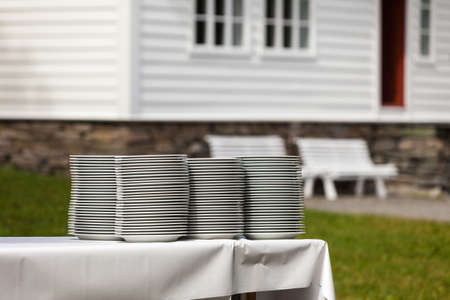Big piles of fresh clean plates drying outside on table with white tableclothの写真素材