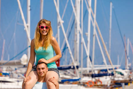 Relationship goals, summer love concept. Man giving girlfriend piggyback ride on marina.の写真素材
