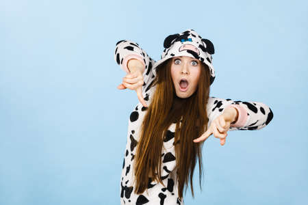 Happy teenage girl in funny nightclothes, pajamas cartoon style pointing down with positive surprised face expression, studio shot on blue. Advertisement conceptの写真素材