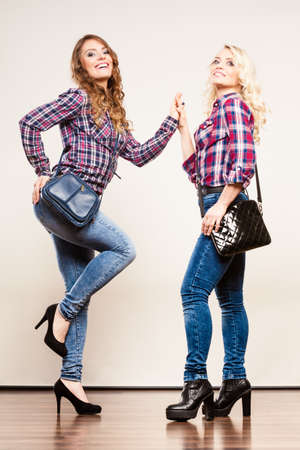 Generation relationship and fashion concept. Adult daughter and mother posing in full length with handbags. Two attractive casual style women wearing denim pants plaid shirtsの写真素材