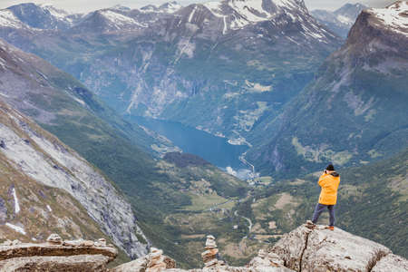 Tourism vacation and travel. Male tourist taking photo with camera, enjoying Geiranger fjord and mountains landscape from Dalsnibba Plateau viewpoint, Norway Scandinavia.の写真素材