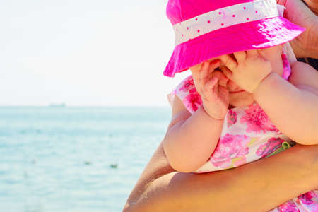 Baby with hat in hands of adult on sunny dayの写真素材