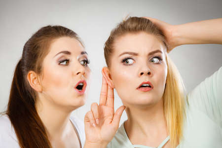 Young woman telling her friend some secrets, two women talking gossiping. Excited emotional girl...