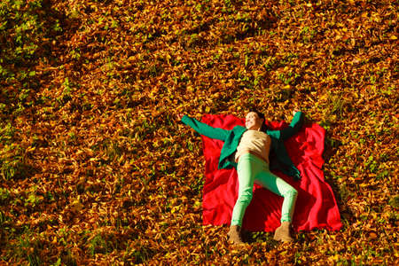 Woman sitting with blanket on autumnal leaves enjoying beautiful autumn weather in park on forest. Many yellow golden leafsの写真素材