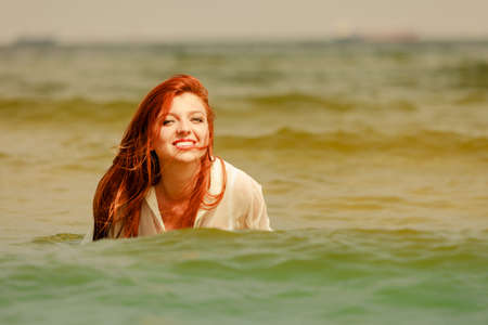 Summer fun, recreation outside concept. Redhead adult woman playing in water during summertime, having great time and smiling joyfullyの写真素材