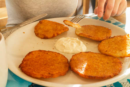 Delicious potato pancakes on plate with sour cream. Traditional slavic dish. Woman hands holding cutleryの写真素材