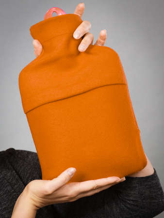 Woman holding warm orange hot water bottle. Fever, flu treatment objects concept.