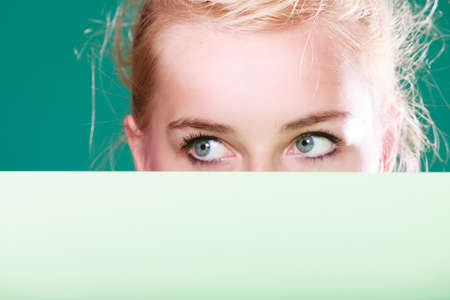 Woman standing behind white board at eye level, half face only. Studio shot on blue green backgroundの写真素材