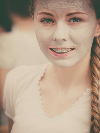 Skincare. Young positive woman with grey clay mud mask on her face. Female taking care of skin condition. Spa beauty treatment. Filtered imageの写真素材