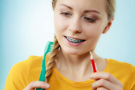 Dentist and orthodontist concept. Young woman with blue braces cleaning and brushing teeth using two...
