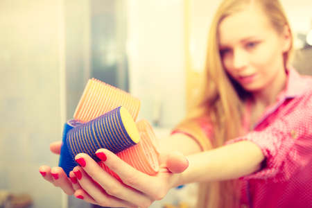 Styling at home concept. Happy woman holding hair rollers in bathroom about to make fancy coiffureの写真素材