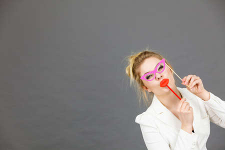 Happy elegant woman holding carnival accessoies on stick having fun at work wearing white office jacketの写真素材