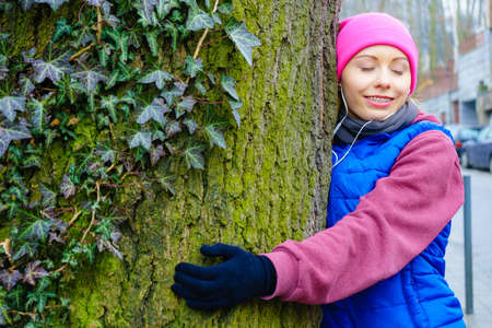 Woman wearing sportswear giving hug embracing tree trunk being in love with nature.の写真素材