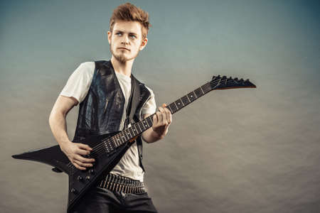 Young bearded man with electric guitar. Adult person is holding instrument and playing. Hobby, music concept, on greyの写真素材