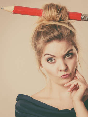 Charming thinking blonde woman having big pencil in hair having something on her mind, education ideas.の写真素材