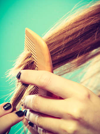 Haircare concept. Female hand combing brown hair with wooden comb on blue greenの写真素材