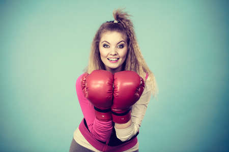 Funny blonde girl female boxer in big fun red gloves playing sports boxing studio shot on blueの写真素材