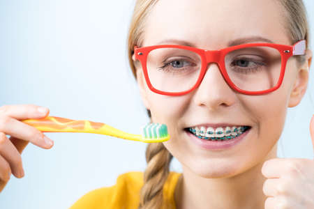 Dentist and orthodontist concept. Young woman smiling cleaning and brushing teeth with braces using toothbrushの写真素材