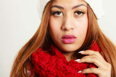 Winter clothing, fashion concept. Closeup of young mulatto woman wearing red woolen scarf. Mixed race girl in wintertime clothes, studio shotの写真素材
