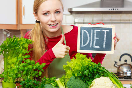 Young woman in kitchen having many green vegetables presenting board with diet sign.の写真素材