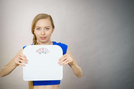Teenage woman holding bathroom scale machine thinking about weight loss and proper body mass. Being...