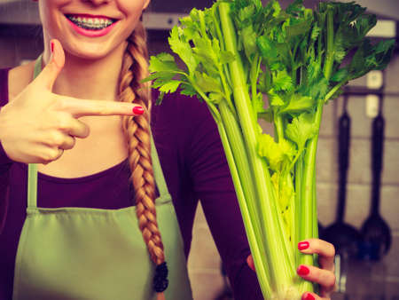 Woman in kitchen holding green fresh stemmed celery. Young housewife cooking. Healthy eating, vegetarian food, dieting and people concept.の写真素材
