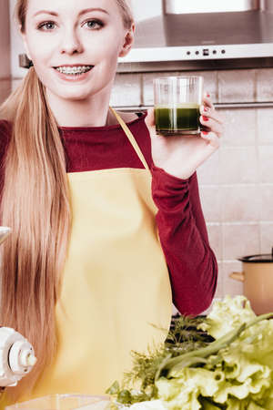 Drinks good for health, diet breakfast concept. Young woman in kitchen holding green healthy vegetable smoothie juice glassの写真素材
