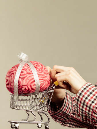 Woman hand holding shopping cart with brain inside. Clever, responsible buying concept.の写真素材