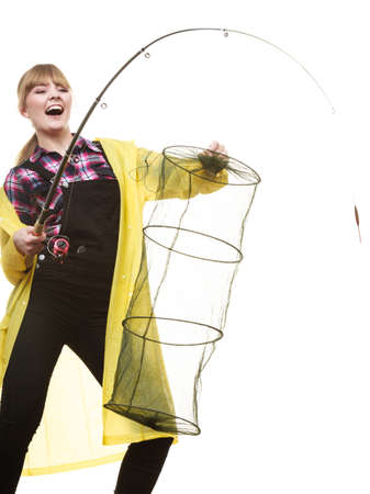 Spinning, angling, cheerful fisherwoman concept. Happy woman in yellow raincoat holding fishing rod and keepnet having fun.の写真素材