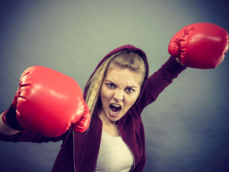 Sporty angry determined woman wearing red boxing gloves, fighting. Studio shot on dark background.