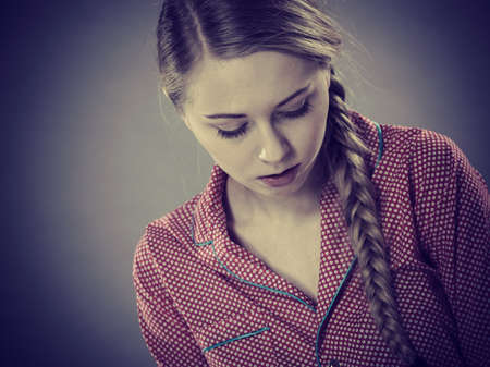 Adolescence problems concept. Sad young teenager woman sitting on bed feeling depressed.の写真素材