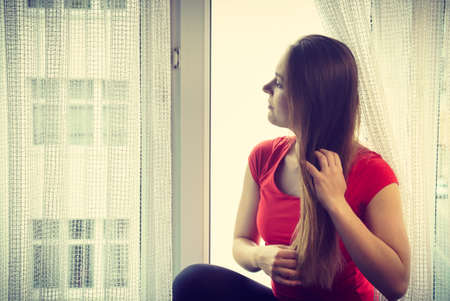 Happy woman sitting on windowsill, energizing morning thinking about day, relaxing having good time.