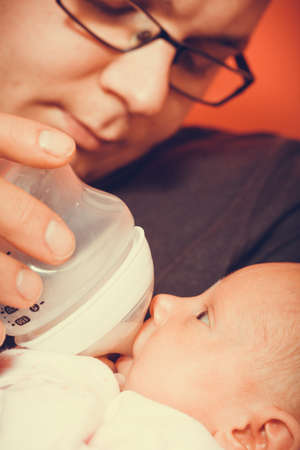 Parenting and love concept. Father holding and taking care of little newborn baby, feeding milk from bottle.の写真素材