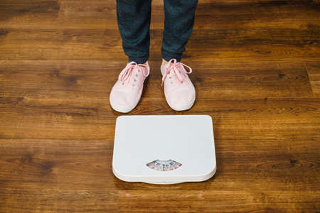 Top view of woman feet wearing pink sneakers on bathroom weight scale. Fit, dieting, fat loss concept.の写真素材