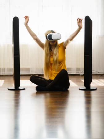 Young woman wearing virtual reality goggles vr box with arms outstretched sitting on floor in living...