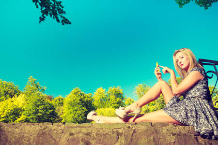 Technology, outdoor relaxation concept. Woman sitting in park, relaxing and using mobile phone, spending her leisure time outsideの写真素材