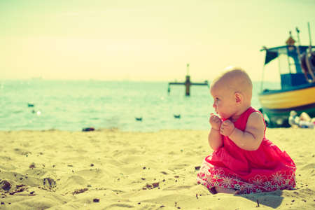 Small child sitting, playing, having fun and trying to eat sand on the beach near the sea.の写真素材