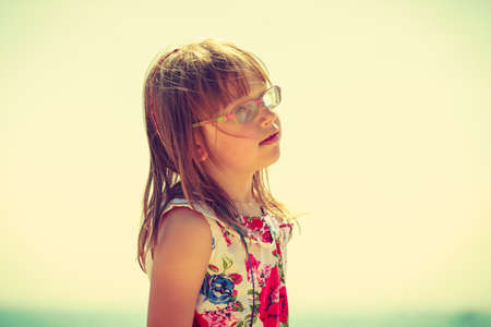 Girl wearing glasses and summeral clothing looks away, light background.の写真素材