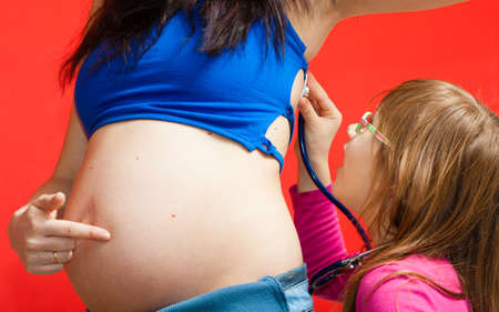 Pregnancy, family concept. Daughter using stethoscope on her pregnant mother, playing and having funの写真素材