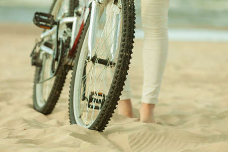 Unrecognizable woman bike cycling on sandy beach. Summer time sport recreation concept.の写真素材