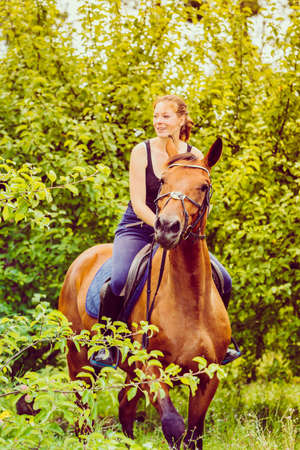Animal, horsemanship concept. Young woman ridding on a horse through garden on sunny spring day