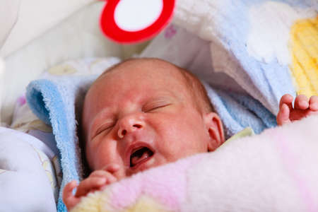 Infant care, teething pain, colic ache concept. Little newborn baby crying in bed surrounded with blanketsの写真素材