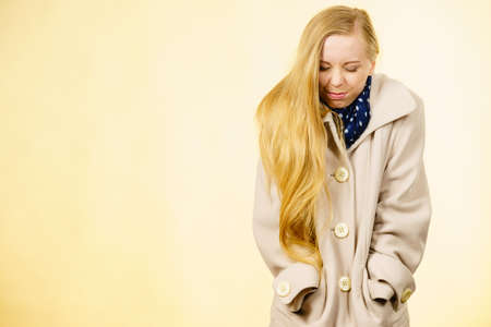 Woman wearing autumnal beige coat feeling cold. Fall overcoats, outfit and fashion concept. Studio shot on yellow backgroundの写真素材