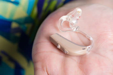 Closeup senior woman with electronic hearing aid in her hand. Health care, hear disorder, device for...