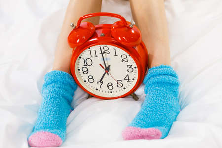 Sleepwear fashion and accessories concept. Woman in pajamas wearing furry warm socks, old fashioned clock next to feet closeupのeditorial素材