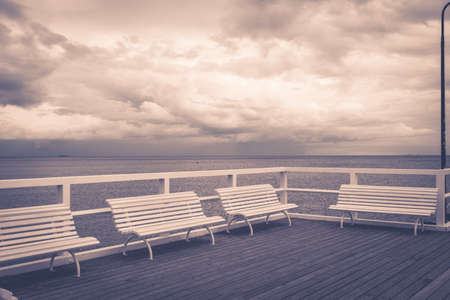 Wooden pier in Sopot with white benches on sea during cloudy rainy weather.の写真素材