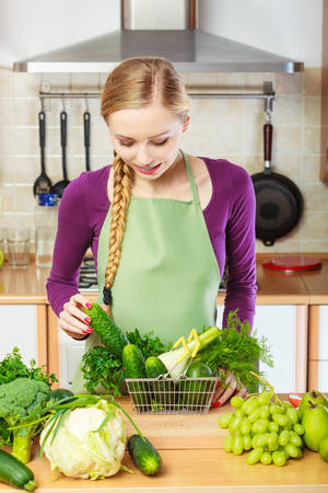 Buying healthy dieting food concept. Woman in kitchen having many green vegetables holding small shopping basket trolley.のeditorial素材
