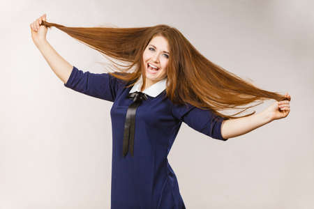 Happy positive woman with long brown hair presenting her healthy hairdo. Haircare concept. Studio shot on grey backgorund.のeditorial素材