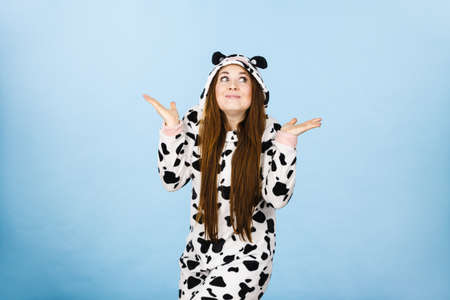 Teenage girl in funny nightclothes, pajamas cartoon style making silly face, shrugging woman in doubt doing shrug, confused girl gesturing do not know sign, studio shot on blue.のeditorial素材