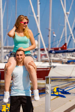 Relationship goals, summer love concept. Man giving girlfriend piggyback ride on marina.のeditorial素材